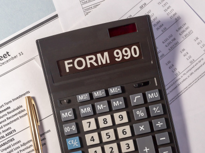 inscription text form 990 on a calculator that lies on business papers and a golden pen on a blue background. USA Tax form concept