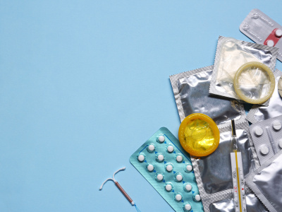 Contraceptive pills, condoms, intrauterine device and thermometer on light blue background, flat lay with space for text. Different birth control methods